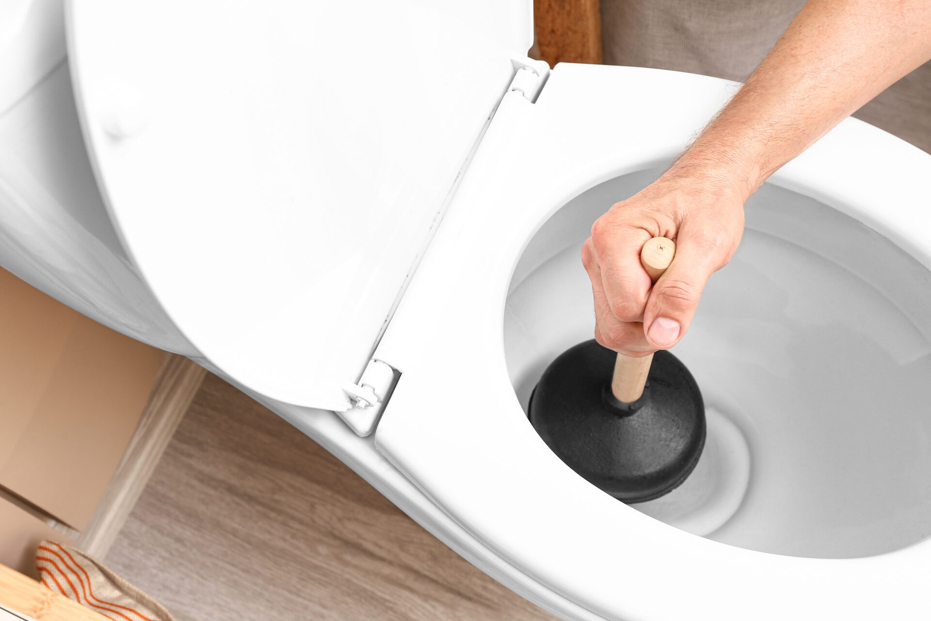 Man using plunger to unclog a toilet bowl